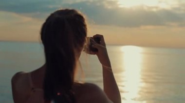 Arkadan görünüm günbatımında nehrin bir resim çekmek güzel bir kız. Smartphone üzerinde fotoğraf çekmek