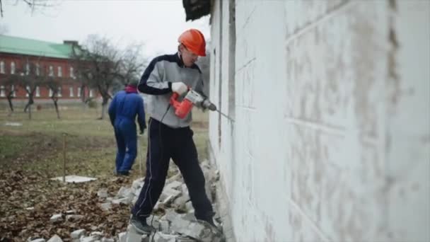 Muž s perforační prolomit zeď venku. Muž v ochrannou přilbu. Bourací práce — Stock video