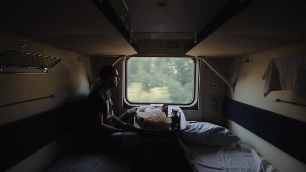 A young male passenger travels in a train carriage in the morning. He looks in the window, and thinks about something. Side view — Stock Video