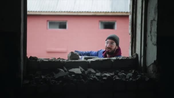 Vue de l'intérieur. Un homme brisant un mur de briques à l'aide d'un marteau. Seul le haut de son corps est vu . — Video