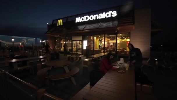 Barcelona, España - 27 de abril de 2018: Una joven pareja comiendo en las mesas de verano de McDonald 's a última hora de la noche. McDonalds restaurante de comida rápida en la carretera. Una parada para descansar y comer durante un camino — Vídeo de stock