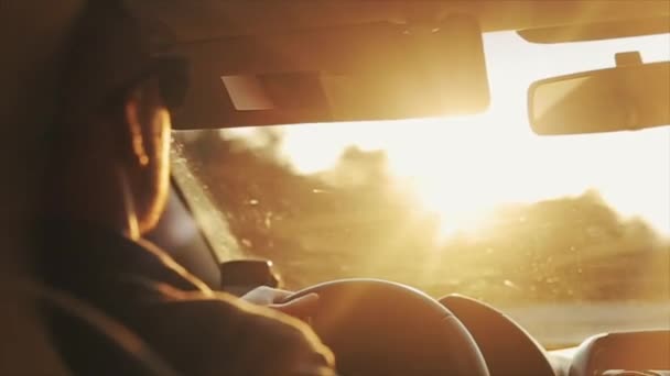 Güneş gözlüklü yetişkin bir adamın gündüz vakti araba sürüşünü yakından izlemek. Parlak güneş gözlerinde parlıyor. — Stok video