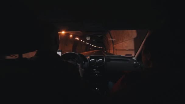 Семейная пара путешествует на машине и проходит через длинный темный автомобильный туннель. Вид с заднего сиденья автомобиля — стоковое видео