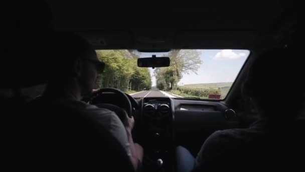 Ein Mann und eine Frau sind mit dem Auto auf der Autobahn unterwegs, auf deren einer Seite ein Wald liegt. Felder am Horizont — Stockvideo