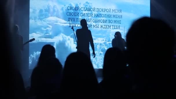 La silhouette di un uomo che canta sul palco. Persone in piedi di fronte al palco in un concerto. Adorazione — Video Stock