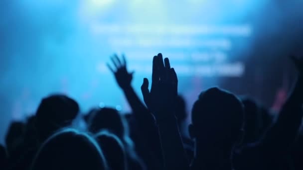 Des gens levant la main à un concert. Un gros plan. Une vue de derrière. Chantant. Scène floue . — Video