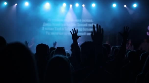 Silhuetas de jovens com mãos levantadas cantando e dançando em um concerto. Vista traseira . — Vídeo de Stock