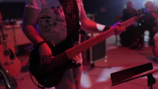 Un joven guapo guitarrista toca en un concierto. Equipo musical y orquesta en el fondo — Vídeos de Stock