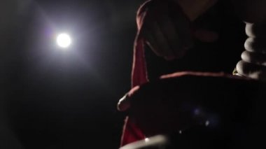Bir close-up sağ elini üzerinden kırmızı bir bandaj unwrapping bir boksör. Kavgadan sonra bir sporcu. Karanlıkta bir spot ışığı