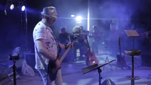 Τον προορισμό Bobruisk, Λευκορωσία - 31 Ιουλίου 2018: Ροκ συναυλία. Ένα νεαρό όμορφος κιθαρίστας παίζει σε μια συναυλία. Μουσικό εξοπλισμό και ορχήστρα στο φόντο — Αρχείο Βίντεο
