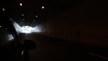 Siyah bir araba uzun bir tünele doğru gidiyor. Soldaki dağlar ile yolda sürüş