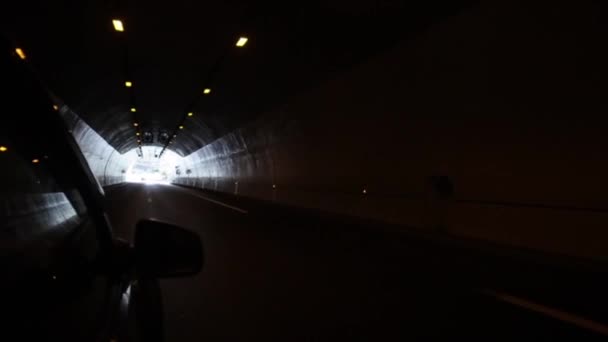 Een zwarte auto gaan door een lange tunnel. Drijven op de weg met bergen aan de linkerkant — Stockvideo