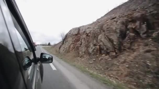 Egy autó, egy kanyargós út a hegyek közelében folyik. Fiatal női utas, szárny tükör tükre. — Stock videók