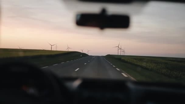 Kör bil längs landsvägen med vindsnurror och stora fält på båda sidorna. Reser i solnedgången — Stockvideo