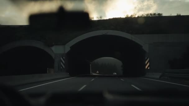 Conduire sous le pont et sortir sur une route de montagne avec une belle vue. Ciel nuageux avec le soleil qui se lève. Vue depuis le pare-brise — Video