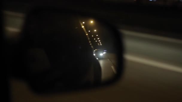 Spiegelung eines fahrenden Fahrzeugs im Außenspiegel. Nachts mit dem Auto unterwegs — Stockvideo