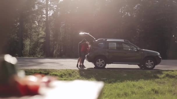 Un jeune homme et une jeune femme prennent quelque chose dans le coffre. Voiture debout sur la route avec du bois sur le fond — Video