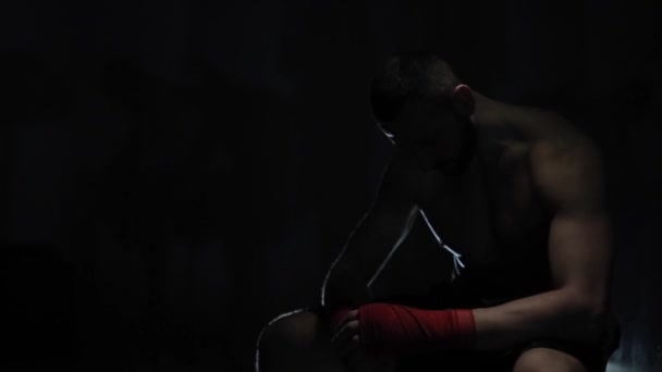 Um atleta masculino bonito preocupado com a cabeça abaixada sentado na escuridão. O jogo da luz. Um pugilista desesperado — Vídeo de Stock