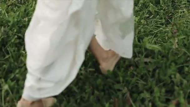 Gros plan d'une mariée dans une longue robe blanche marchant sur l'herbe — Video