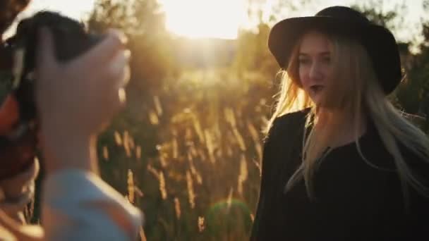 Vista cercana de una modelo femenina y una fotógrafa divirtiéndose y bailando durante la sesión de fotos en el campo al atardecer — Vídeo de stock