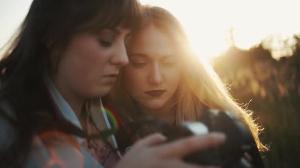 Dos hermosas chicas están buscando fotos en la cámara digital exterior. Una vista cercana — Vídeo de stock