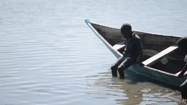 Kenya, Kisumu - 2017. május 20.: Afrikai fiúk a csónakban ül, és elhelyezés a lábukat a vízben, a tó. — Stock videók