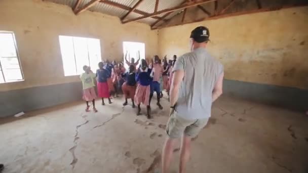 Kenia, Kisumu - 20 mei 2017: Blanke mannen dansen met Afrikaanse kinderen binnen het schoolgebouw. — Stockvideo