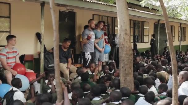 Kenya, Kisumu - 20 maj 2017: Kaukasiska män står och pratar i afrikanska skolan till grupp barn. — Stockvideo