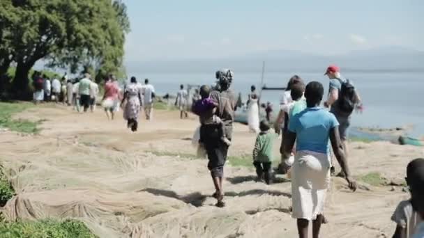 Kenia, Kisumu - 20 mei 2017: Groep Afrikaanse en Kaukasische mensen met kinderen lopen op de oever van de zee. — Stockvideo