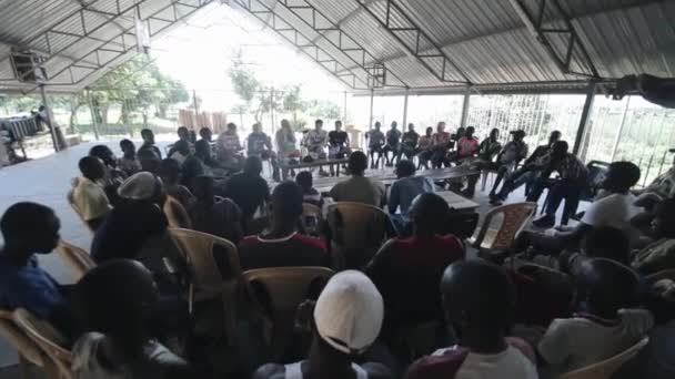 Kenya, Kisumu - 20 Mayıs 2017: Grup Afrika insanlar daire içinde oturan ve beyaz erkekler, gönüllüler için dinleme. — Stok video