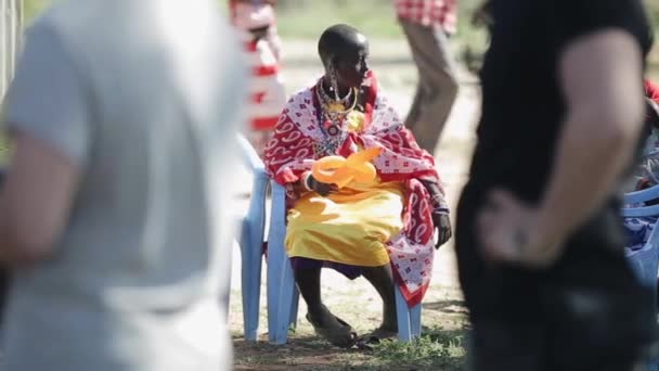 Kenya, kisumu - 20. Mai 2017: alte afrikanische Frau vom örtlichen Massai-Stamm sitzt auf Stuhl und hält Luftballon. — Stockvideo