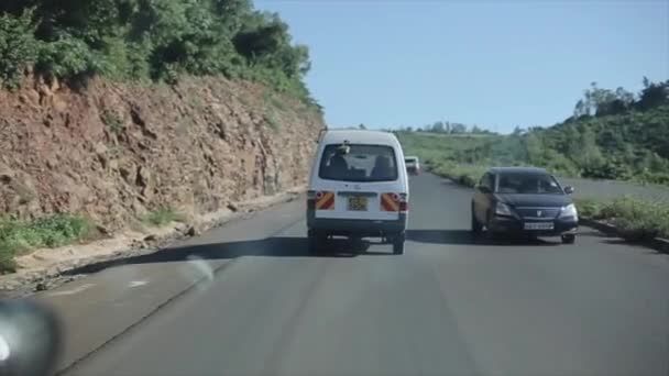 Kenia, Kisumu - 20 mei 2017: Uitzicht vanaf binnen een rijdende auto na een busje. Auto rijdt via de landweg, op serpentine in stralende dag in Afrika. — Stockvideo