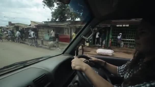 KENIA, KISUMU - 20 DE MAYO DE 2017: Vista a través del parabrisas desde el interior de un coche.La mujer está conduciendo a través de la ciudad en África en un día soleado y brillante . — Vídeo de stock