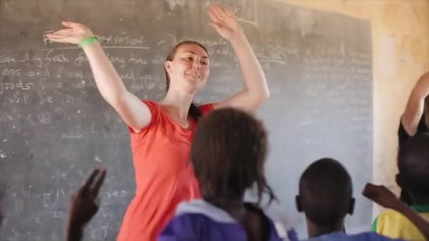 Kenia, Kisumu - 20 mei 2017: Jonge mooie Kaukasische vrouwen dansen met Afrikaanse kinderen in lokale school. — Stockvideo