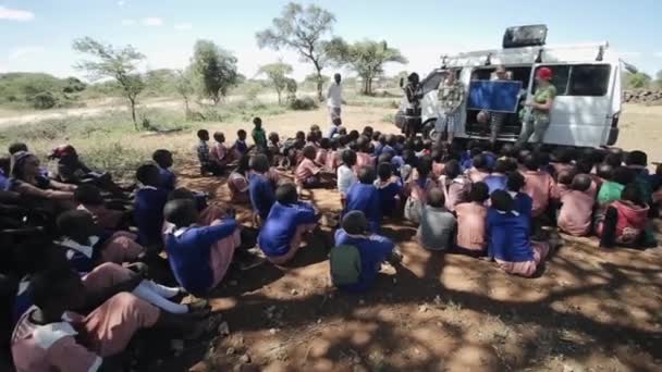 KENYA, KISUMU - MAIO 20, 2017: Crianças africanas sentadas no chão e ouvem homens e mulheres caucasianos . — Vídeo de Stock