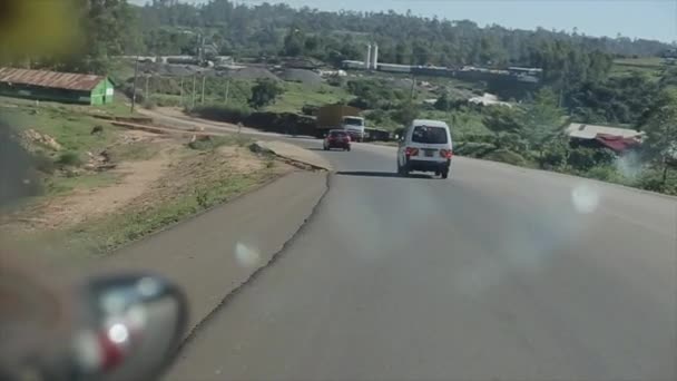 Visa genom en vindruta från inuti en bil. Van går igenom en landsväg nära African village, buss passerar nära bilväg. — Stockvideo