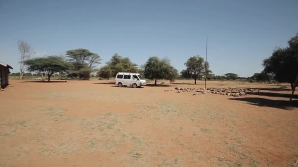 Un furgone bianco che attraversa il campo in Africa. Bambini in piedi vicino alla scuola locale . — Video Stock