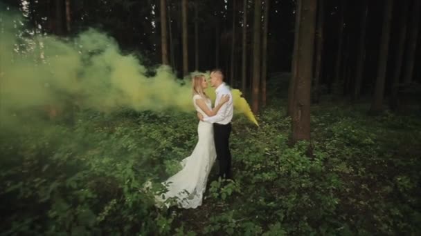 Glückliches Hochzeitspaar umarmt und küsst sich im Wald mit gelbem Rauch im Hintergrund — Stockvideo