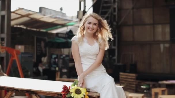 Retrato de uma jovem noiva bonita sentada e sorrindo ao ar livre. Movimento lento — Vídeo de Stock
