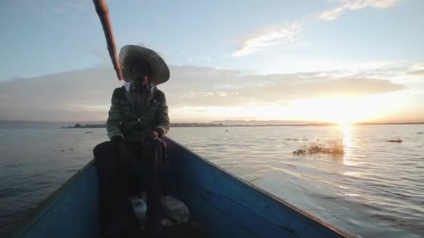 African fisherman is sitting in boat at dawn. Young man in straw hat goes to sea in morning. — Stock Video
