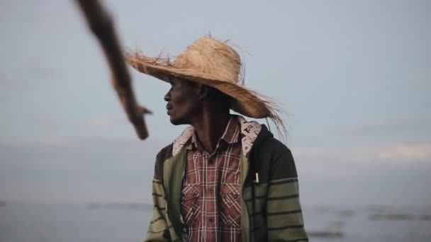 Hasır şapkalı Afrika balıkçı portresi. Tekne ve yakalar balık yalnız oturan genç adam. — Stok video