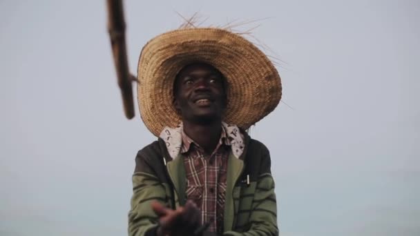 Portrait de jeune homme africain assis dans un chapeau de paille dans le bateau et parlant, montrant à la main . — Video