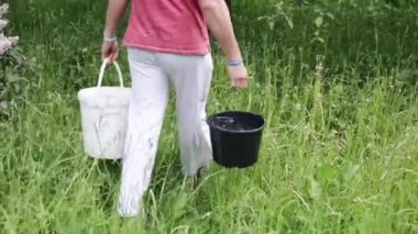 Bir adam iki kova su taşıyan ve sonuçta koyuyorum. Beyaz bir kova. Siyah bir kova. 2 tam kova su. Bahçede