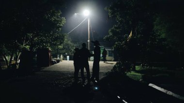 Kenya, Kisumu - 20 Mayıs 2017: Bir grup insan yolda gece geç saatte ayakta ve konuşmak. Afrika adam şapkalı Afrika bir köyden. Lamba parlak karanlıkta parlar. Köyü