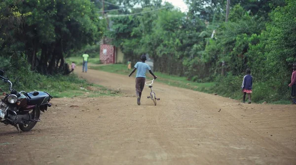 KENIA, KISUMU - 20 DE MAYO DE 2017: Vista trasera del niño caminando por la carretera en África. Hombre con bicicleta caminando en el bosque . — Foto de Stock