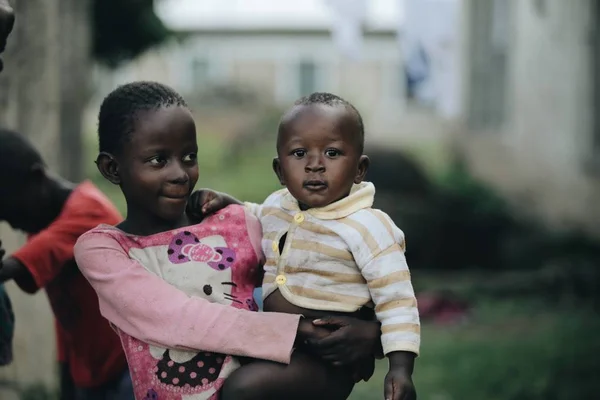 KENIA, KISUMU - 20 DE MAYO DE 2017: Vista trasera de una niña africana llevando a un bebé desnudo por el pueblo . — Foto de Stock