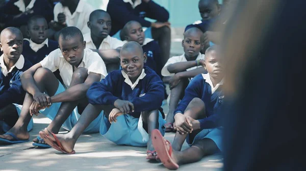 KENYA, KISUMU - MAIO 20, 2017: Grupo de crianças africanas sentadas no chão. Meninos e meninas de uniforme passar o tempo fora . — Fotografia de Stock