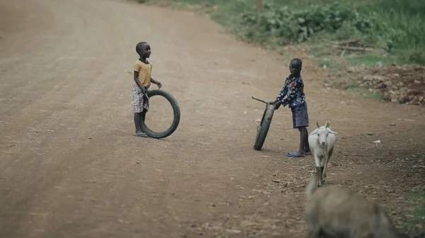 KENIA, KISUMU - 20 DE MAYO DE 2017: Dos chicos africanos jugando con neumáticos en la carretera. Niños divirtiéndose juntos — Foto de Stock