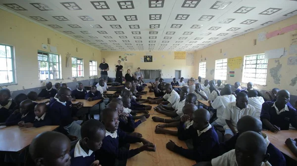 KENYA, KISUMU - MAIO 23, 2017: Grande grupo de crianças e adolescentes africanos sentados, voluntários caucasianos ajudam a fazer pulseiras — Fotografia de Stock