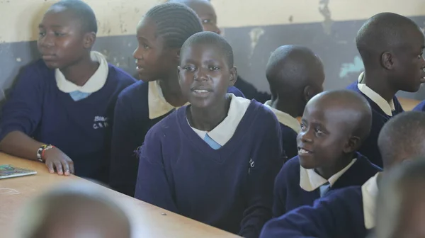 KENYA, KISUMU - 23 de maio de 2017: Grupo de crianças africanas sentadas em sala de aula e olhando para a câmera. Pequeno menino palmas mãos . — Fotografia de Stock